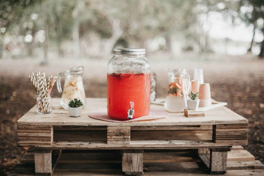 Dispensador de ponche rosado de fresa y jarras de agua en la mesa de bebidas