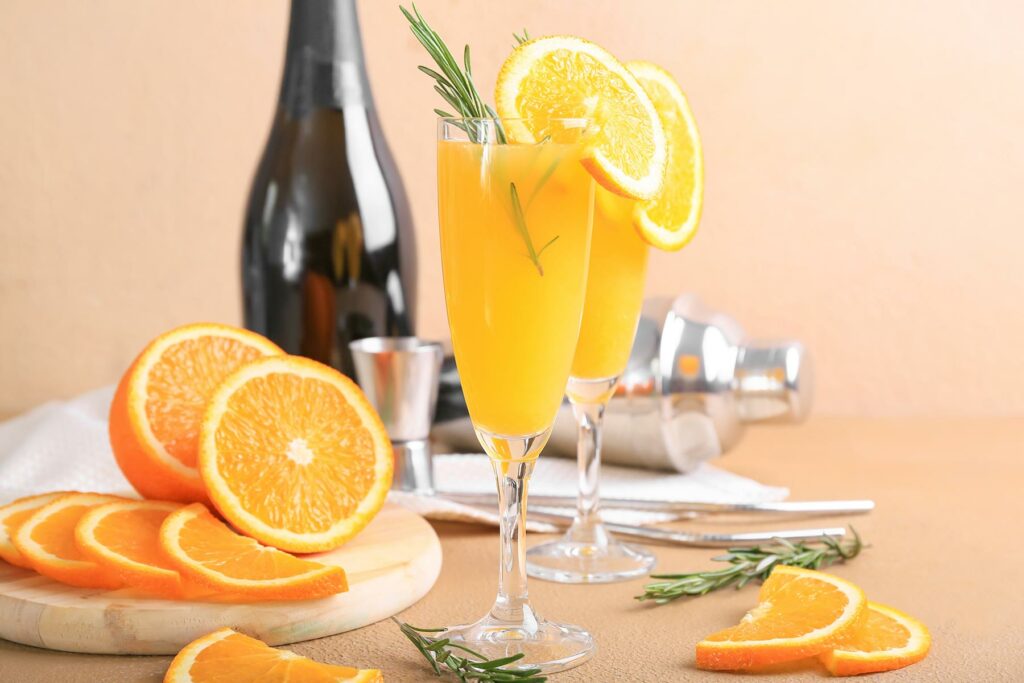Dos mimosas adornadas con rodajas de naranja frente a una botella de champán
